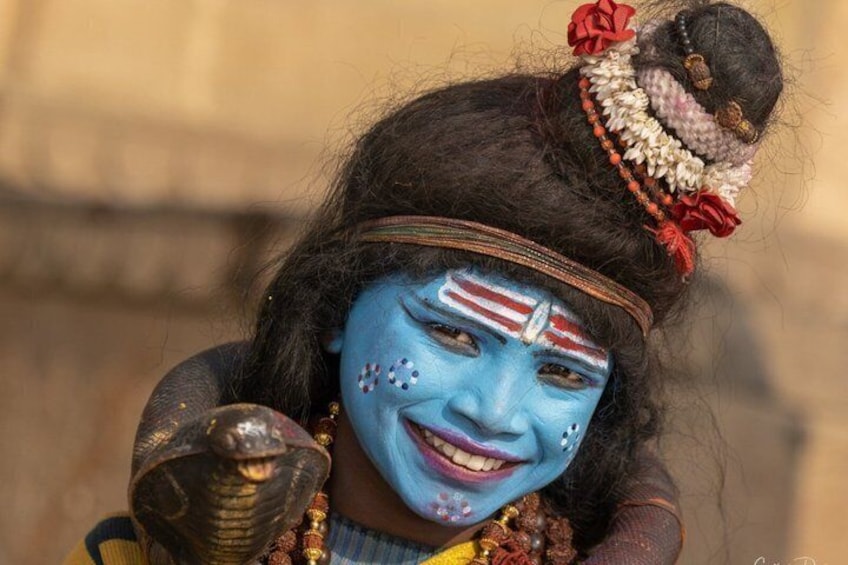 A person with blue face paint, a snake, and traditional attire. 1