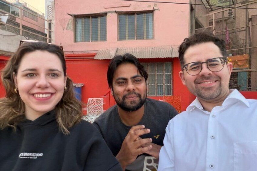 Three people standing in front of a red building with a corrugated roof and a window with a metal grid. 5