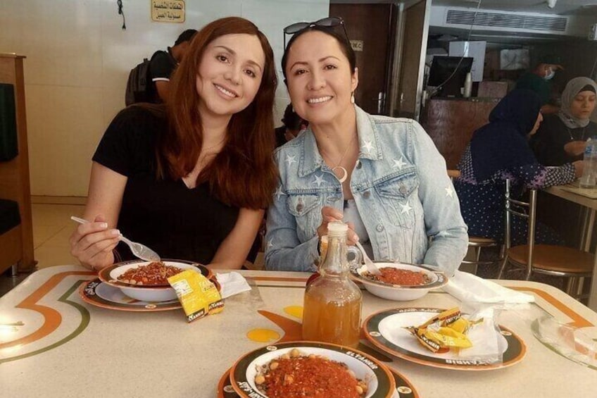 Two people sitting at a table with plates of food, a bottle, and a jug. 5