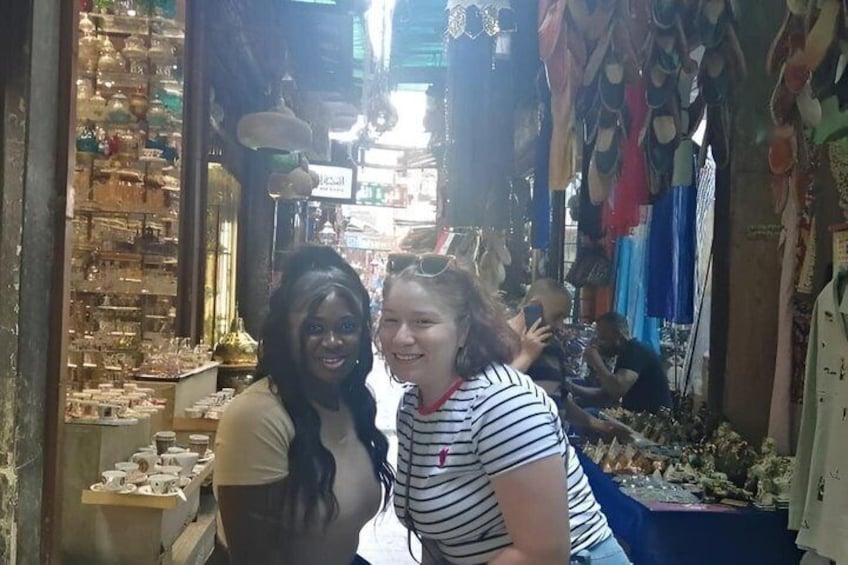 A narrow market alley with stalls selling various items, including jewelry and clothing. 4