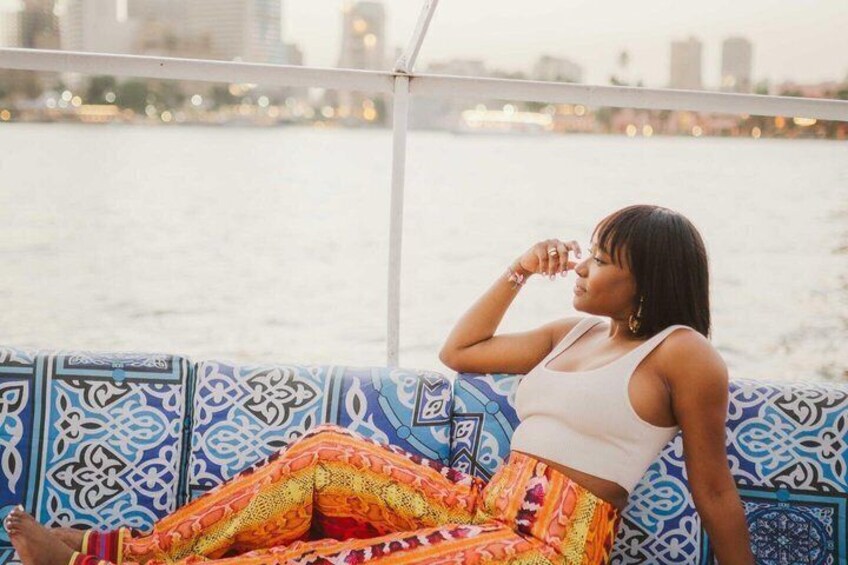 A person sitting on a patterned bench by a body of water with a cityscape in the background. 1
