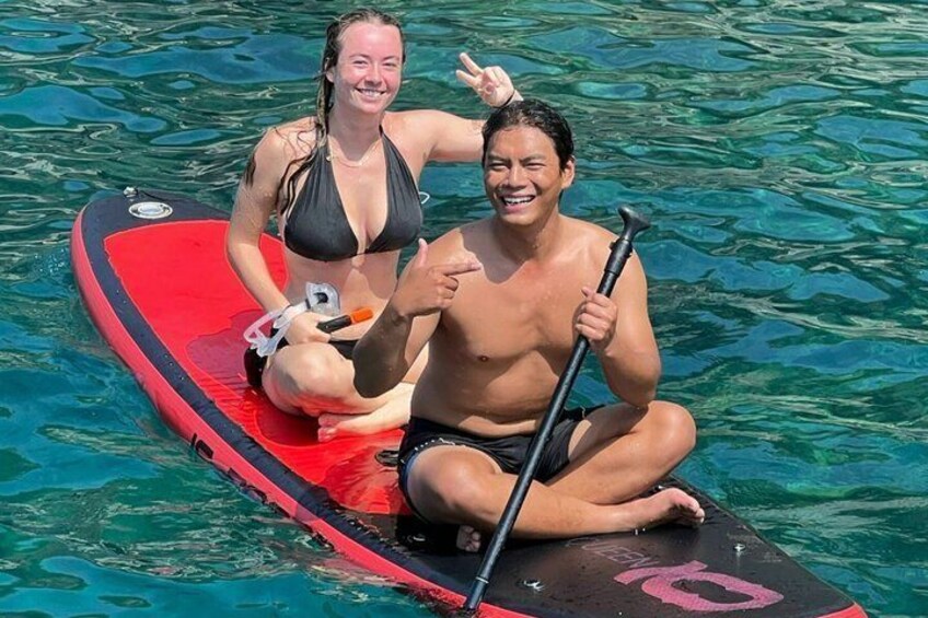 Zwei Personen auf einem roten Stand-Up-Paddle in klarem Wasser. 2