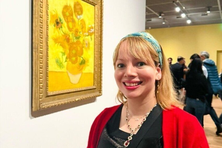 Een persoon staat in een kunstgalerie, op de muur hangt een schilderij van bloemen. 1