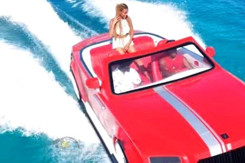Un coche descapotable rojo con una mujer vestida de blanco conduciendo sobre el agua. 3