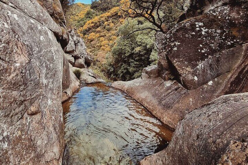 Ein schmaler Fluss zwischen großen Felsen mit einem bewaldeten Hang im Hintergrund. 3