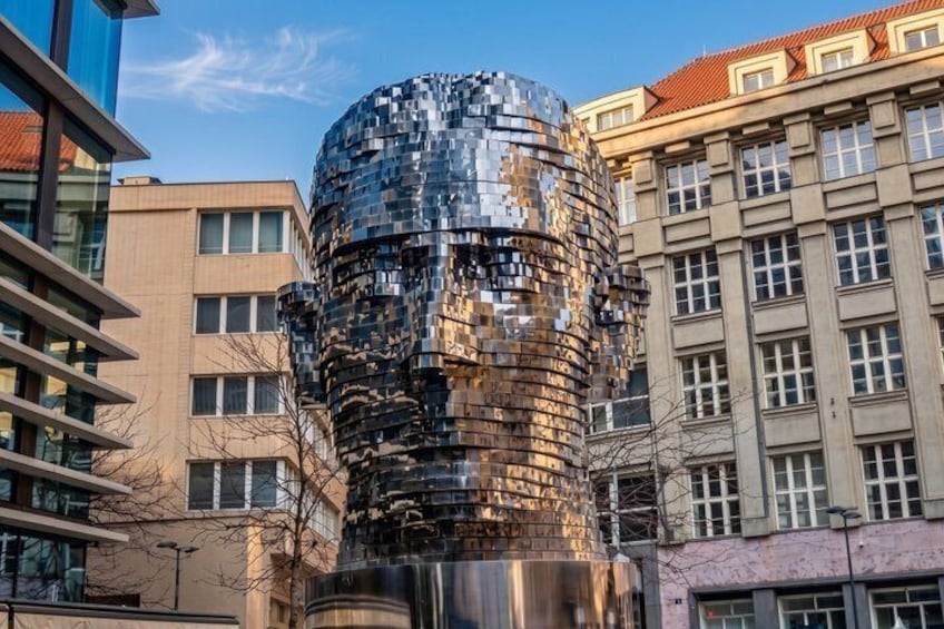 A metallic sculpture with a reflective surface, set against a backdrop of modern buildings and a clear sky. 5