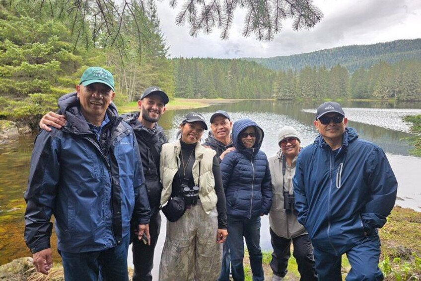 A group of people standing by a lake surrounded by trees. 3