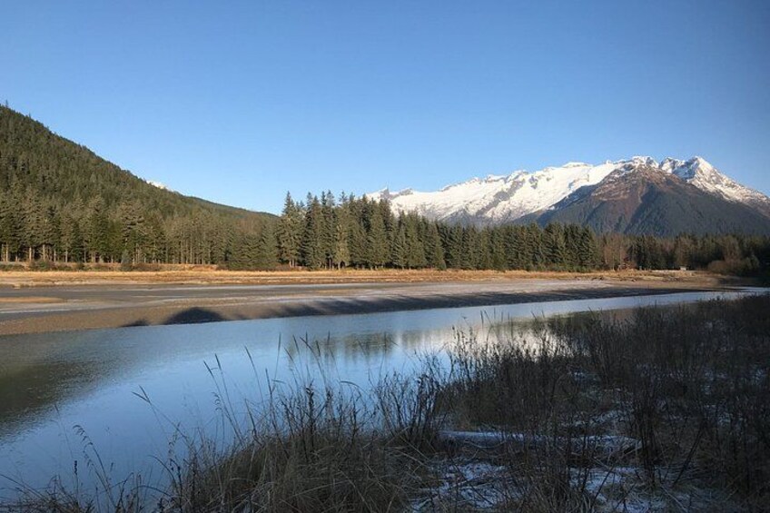 A calm lake with snow-capped mountains in the background and a forested hillside. 2
