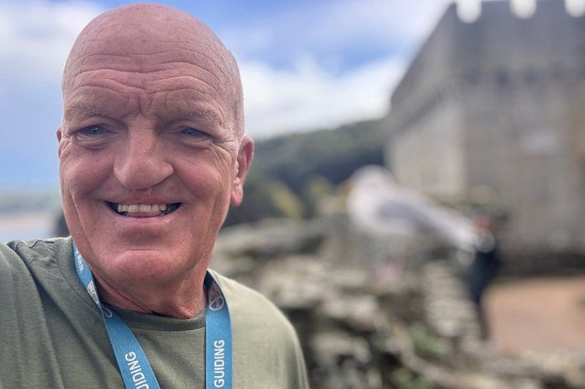 A man with a lanyard, a stone wall, and a building in the background. 5