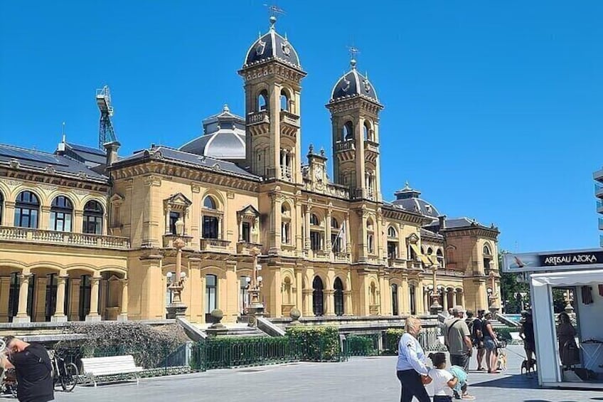 A historic building with two towers, a fountain, and a pedestrian area with people. 1