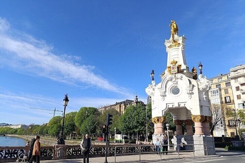 A white monument with a golden statue on top, surrounded by a fence and trees. 3