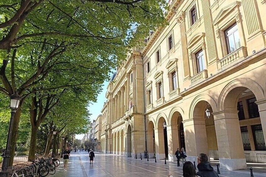 A tree-lined pedestrian street with classical architecture and a few people walking. 2