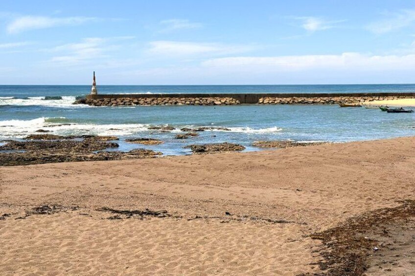 A sandy beach with a rocky breakwater and a lighthouse in the distance. 5