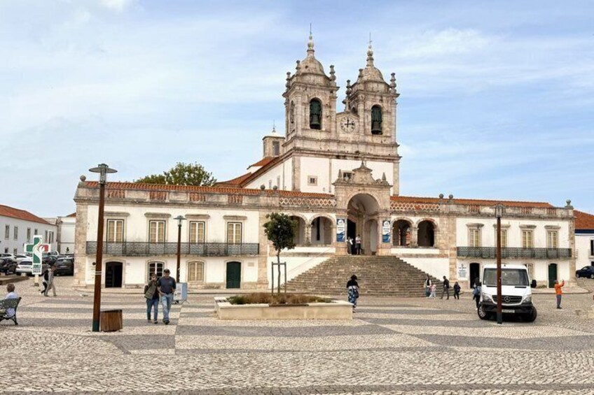 A historic church with a bell tower, cobblestone plaza, and people walking. 3