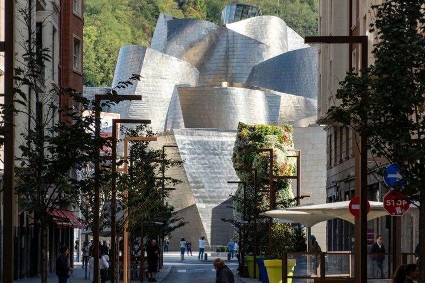 A modern building with a unique geometric facade, surrounded by urban streets and pedestrians. 1