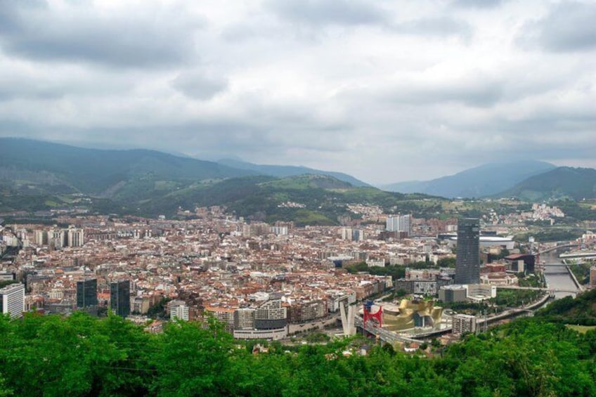 A cityscape with a prominent tower, dense urban buildings, and surrounding hills. 2