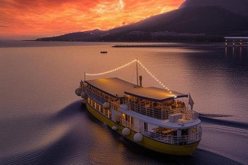 A large boat with a covered deck, anchored in calm waters during sunset. 1