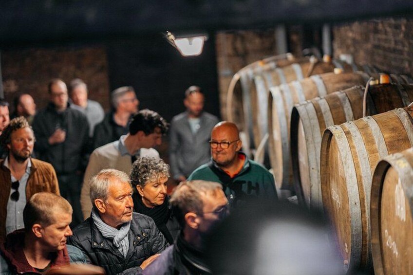 A group of people observing wooden barrels in a dimly lit room. 1