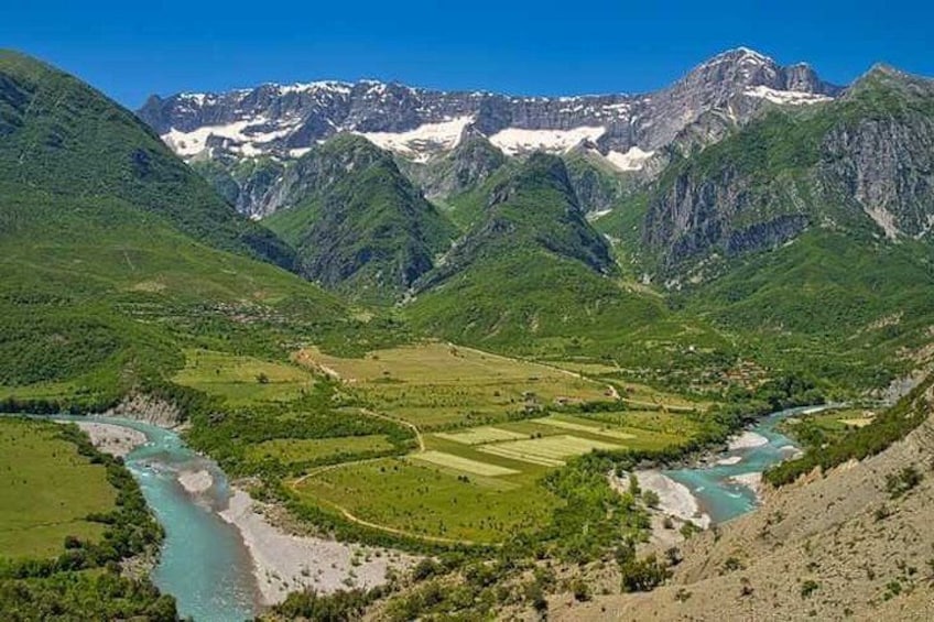 A mountainous landscape with a river, green fields, and snow-capped peaks. 5