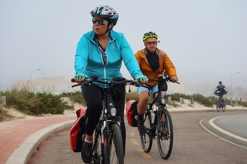 Two cyclists on a road with a red bike lane, surrounded by vegetation and a cloudy sky. 4