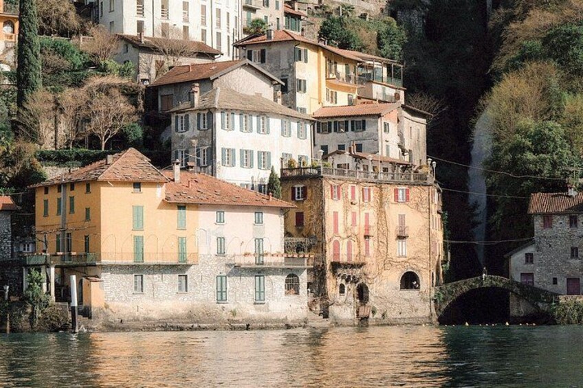 A riverside town with colorful buildings, a bridge, and a steep hillside. 2