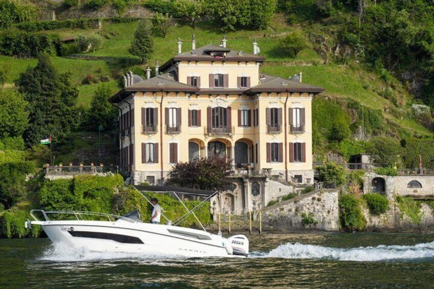 A white boat speeding past a large, yellow building with a hill in the background. 2
