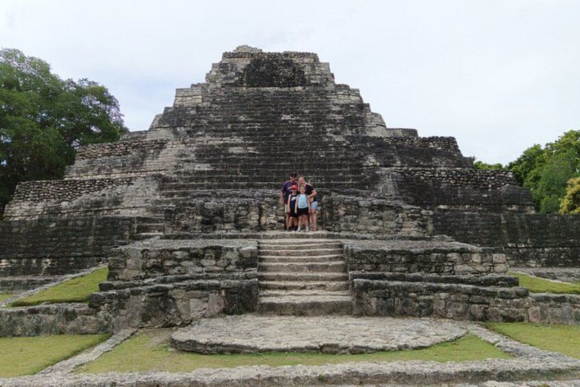 Une structure en forme de pyramide, avec des marches menant à une plateforme, le tout entouré de zones herbeuses. 2
