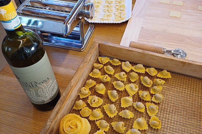 A bottle of wine, pasta sheets, and a pasta maker on a wooden table. 1