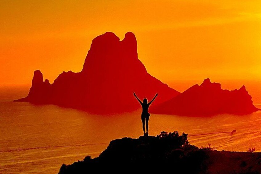 A person standing on a cliff with arms raised, overlooking a mountainous landscape during sunset. 1