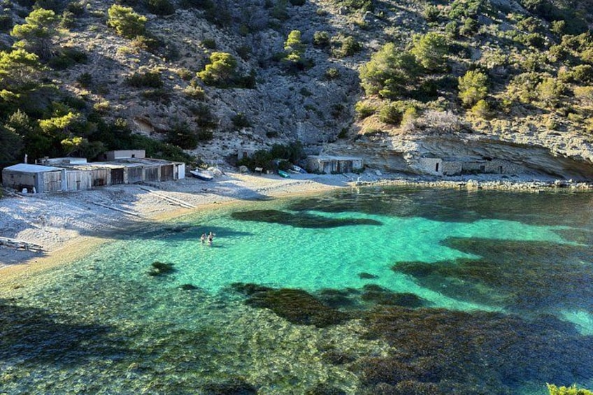 A coastal area with clear turquoise waters, rocky terrain, and small buildings. 3