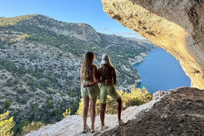 Two people standing on a rocky cliff overlooking a valley and a body of water. 4