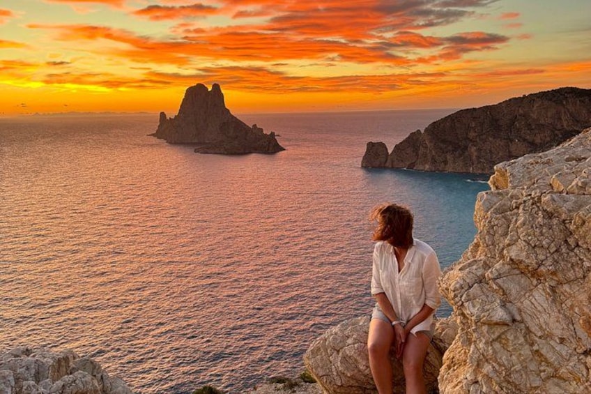 A person sitting on a rocky outcrop overlooking a body of water with a prominent rock formation in the distance during sunset. 5