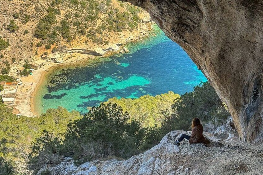 A person sitting on a cliff overlooking a turquoise sea with a rocky coastline and sparse vegetation. 2