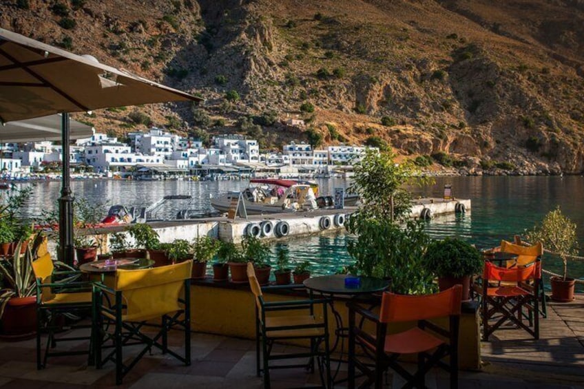 A coastal outdoor seating area with tables and chairs, overlooking a harbor with boats and a hillside village. 5