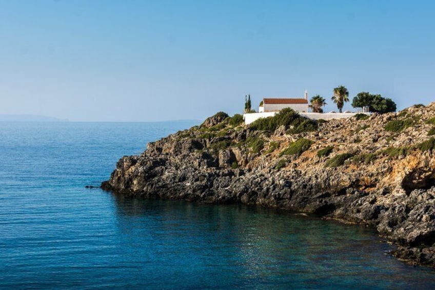A coastal landscape with a rocky cliff, clear blue sea, and a white building with a red roof. 3