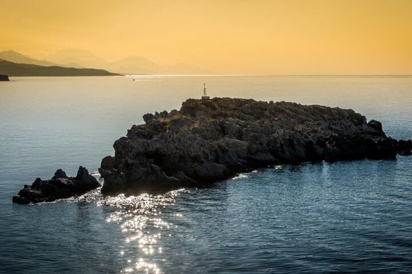 A rocky island with a lighthouse in the distance during sunset. 4