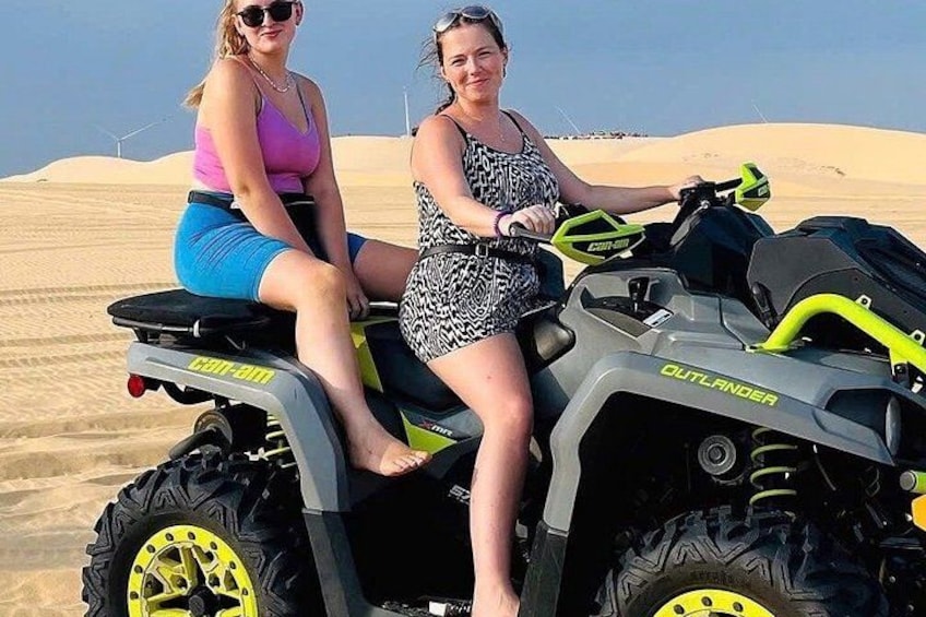 Two people on a quad bike in a desert with sand dunes in the background. 2
