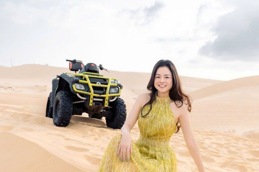 Una persona con un abito giallo seduta sulle dune di sabbia, con un quad sullo sfondo. 5