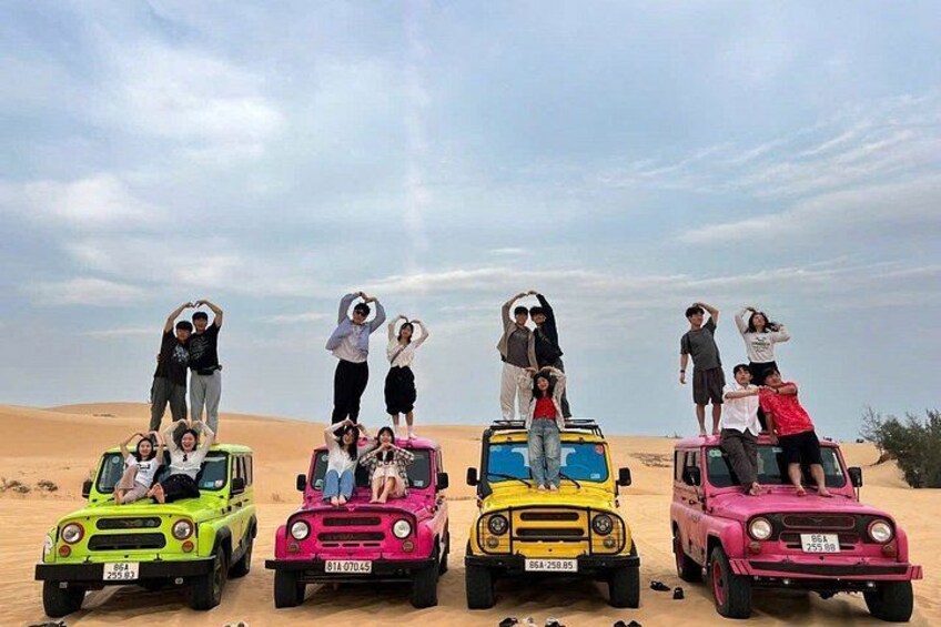 A group of people posing on top of four colorful off-road vehicles in a desert landscape. 1