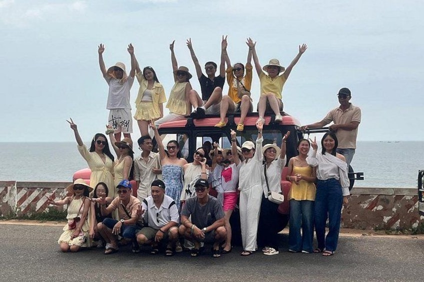 A group of people posing on a vehicle by the seaside. 4