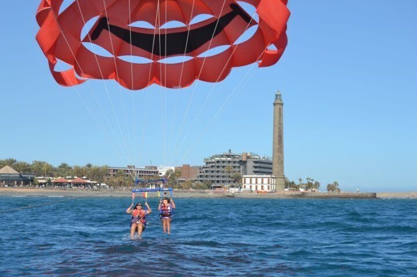 Deux personnes pratiquent le parachute ascensionnel au-dessus d’eaux calmes, avec une vue sur le paysage urbain côtier en arrière-plan. 5