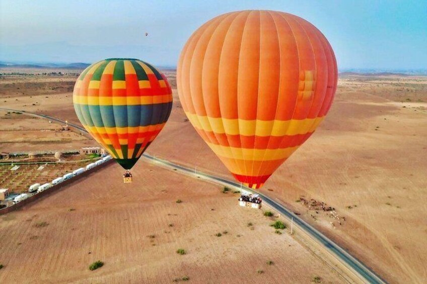 Dos globos aerostáticos sobre un paisaje desértico con una carretera y vegetación escasa. 1