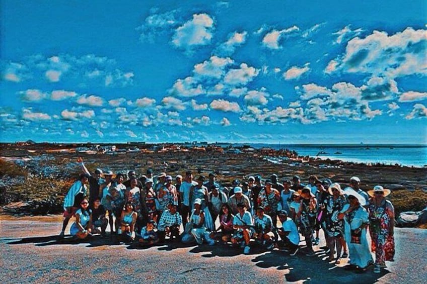 A group of people gathered on a coastal road with a view of the ocean and a clear sky. 2