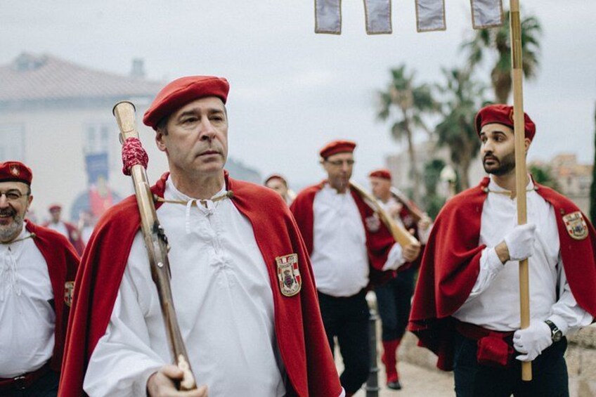 Een groep mensen in rode uniformen met vlaggen en een staf lopen in een rij. 4
