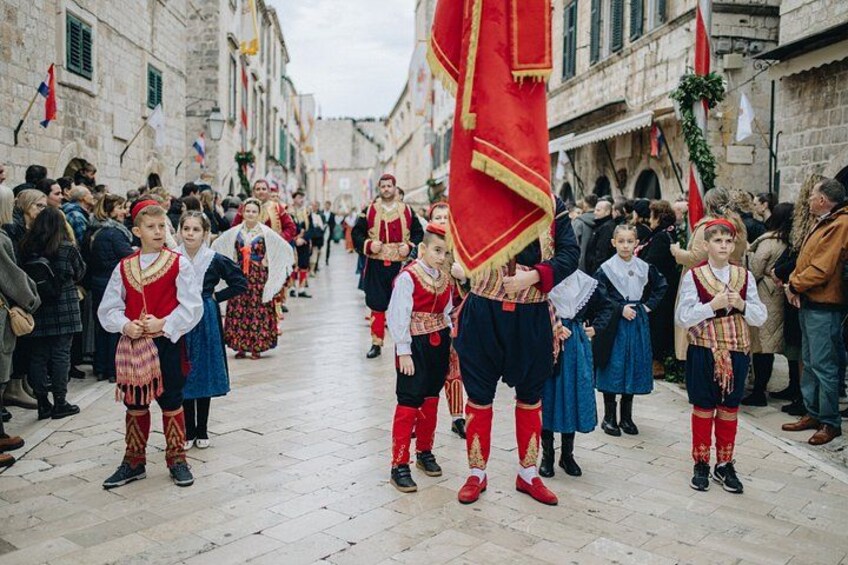 Een groep mensen in traditionele kostuums loopt over een straat. 3