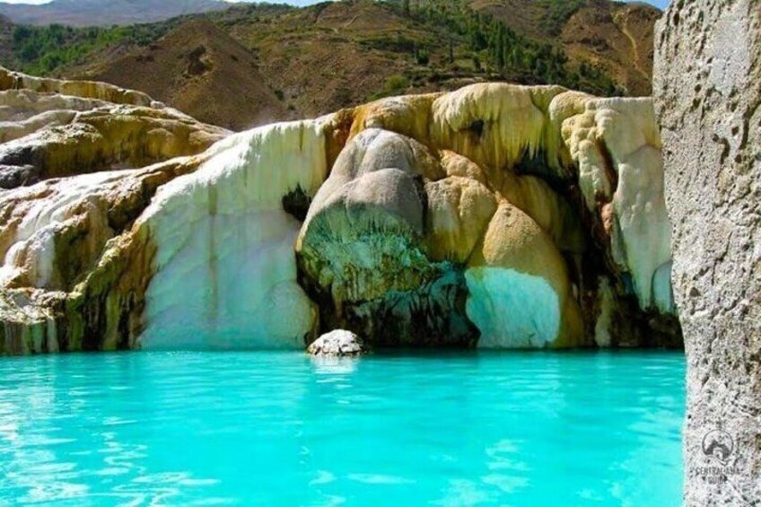 A turquoise pool with mineral deposits and a large rock formation. 1