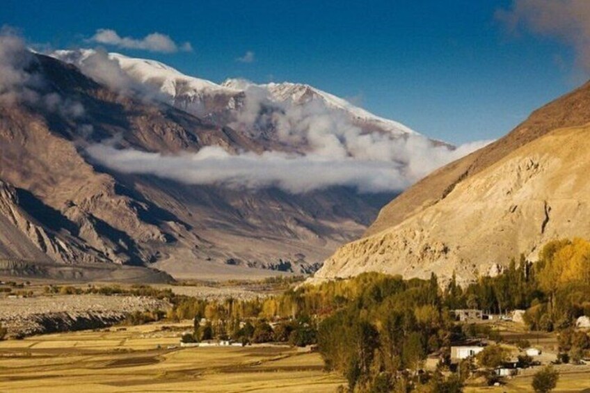 A mountainous landscape with a snow-capped peak, a valley with sparse vegetation, and a small settlement. 2
