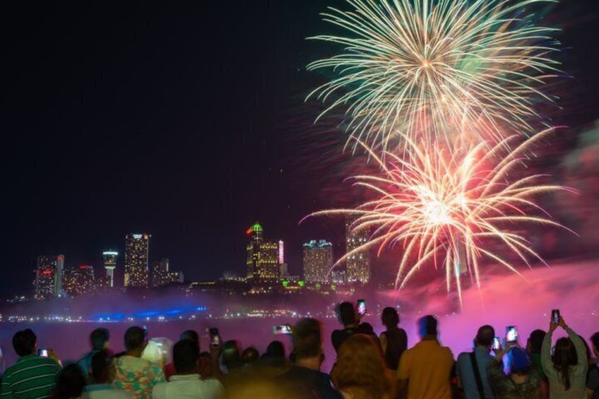 A nighttime cityscape with fireworks over a crowd. 1