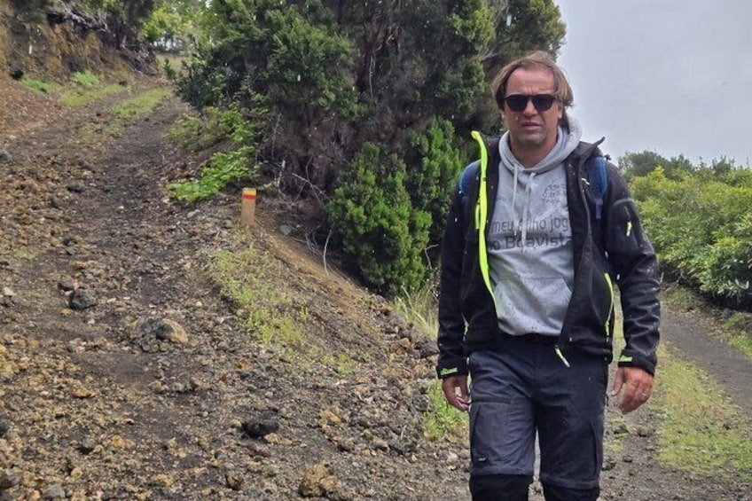 Una persona camina por un sendero rocoso flanqueado por follaje. 1