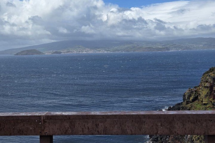 Vista costera con un promontorio rocoso, mar tranquilo y una masa de tierra distante bajo un cielo nublado. 5